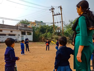 DISTRICT KATNI, INDIA - 17 HAZİRAN 2020: Hint anaokulu öğrencileri toprak sahası spor sahasında bayan öğretmenle oyun oynuyorlar.
