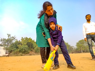 DISTRICT KATNI, INDIA - 17 HAZİRAN 2020: Hintli anaokulu öğretmeni küçük erkek çocuğa kriket oyununu birlikte spor sahasında öğretiyor.