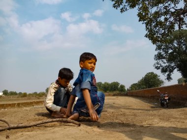 DİSTRİK BILASPUR, Hindistan - 25 Şubat 2020: Gökyüzü arka planında toprak alanda birlikte oynayan iki küçük Hintli çocuk.