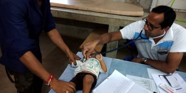 DİSTRİK KATNI, INDIA - 18 Eylül 2019: Hint devlet hastanesi erkek doktoru masadaki yeni doğan bebeğin kalp atışlarını kontrol ediyor.