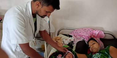 DİSTRİK KATNI, INDIA - 28 Eylül 2019: Hintli bir erkek doktor şehir hastanesinde annesiyle birlikte yeni doğan bebeği yatakta kontrol ediyor.
