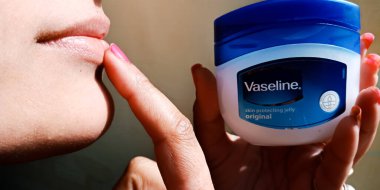 DISTRICT KATNI, INDIA - DECEMBER 30, 2019: an indian girl applying Vaseline moisturizing cream on lips. clipart