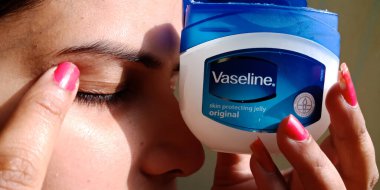 DISTRICT KATNI, INDIA - DECEMBER 30, 2019: an indian girl applying Vaseline moisturizing cream on eyelid. clipart
