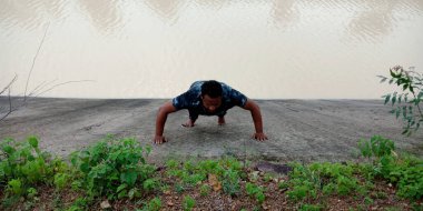 DISTRICT KATNI, INDIA - Eylül 02, 2019: Su kanalı destekli arka plan üzerinde egzersiz yapan Hintli bir çocuk.