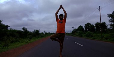 DİSTRİK KATNI, INDIA - 5 Ağustos 2019: Bir Hint köylüsü Yoga duruşu ile karayolu arka planında duruyor.