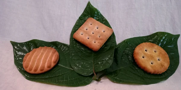 Smakelijk Gezouten Biscuit Weergegeven Verse Groene Glanzende Natuurlijke Bladeren Met — Stockfoto