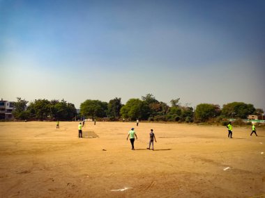 Mavi gökyüzü arka planında toprak tarlasında kriket oynayan Hintliler.