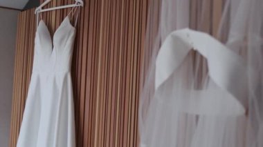 Kahverengi duvarda asılı beyaz gelinlik. Alışılmadık görünüm