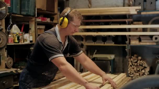 ワークショップにカーペンター 人は木の材料と働く 建設材料や木製の家具を生産するためにワークショップで木工に取り組んで大工 若い大工はプロの道具を使う — ストック動画