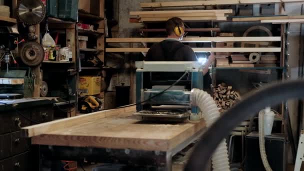 ワークショップにカーペンター 人は木の材料と働く 建設材料や木製の家具を生産するためにワークショップで木工に取り組んで大工 若い大工はプロの道具を使う — ストック動画