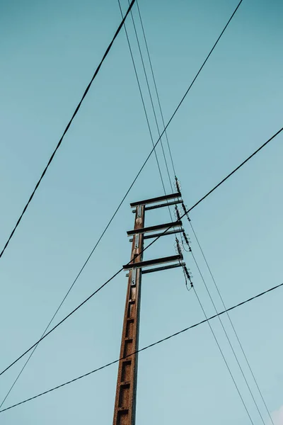 A electrical post with a lot of wires crossing the image and a blue sky