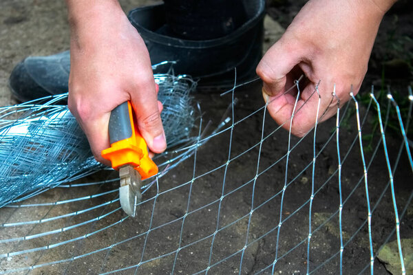 male hand repairing using cutter cutting wire mesh grid with plie, wire cutters