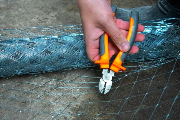 male hand repairing using cutter cutting wire mesh grid with plie, wire cutters