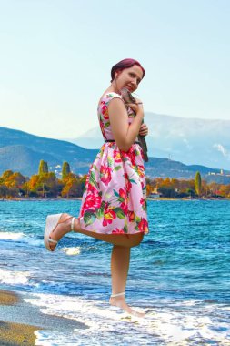 Pembe elbiseli gülümseyen bir kadın büyük kahverengi bir yayın balığı tutuyor. Kedibalığıyla mutlu bir kadın yakaladı.