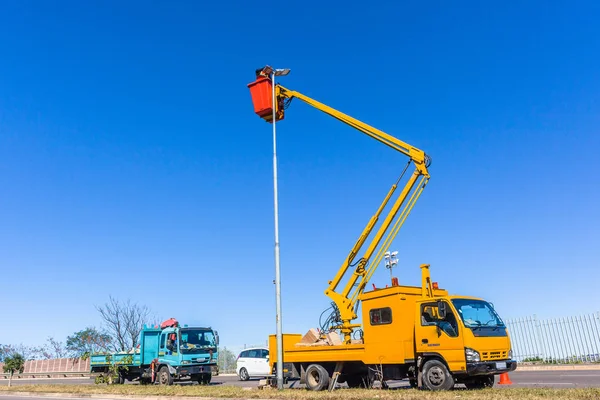 青空に極電球のメンテナンス修理を行うトラック車両から拡張油圧アーム バケットの電気技師を高 — ストック写真