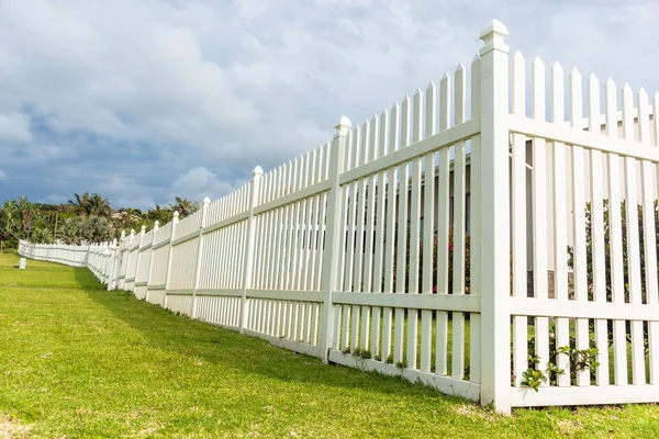 White boundary vertical slat plastic pvc fence along roadside grass landscape.