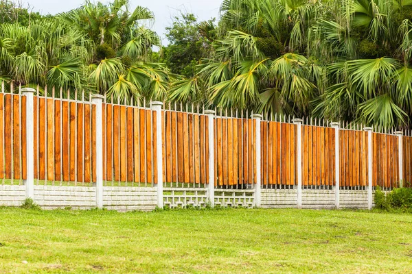 Boundary wall fence contructed with concrete vertical columns steel and wood slats with palm trees.