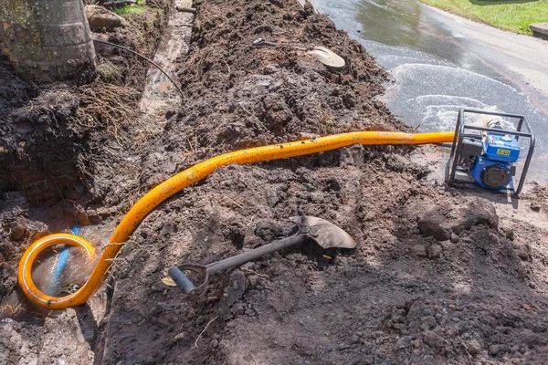 Plumbing earthwork trench digging repairs of broken main water pipe in residential road area with mobile motor pumping  vacuum draining damage.