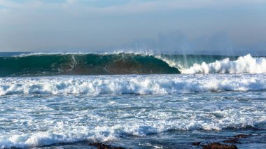 Okyanus dalgası mavi ve beyaz sudan oluşan dik bir duvar sığ resif kumsallarına çarpıyor. .