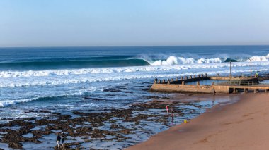 Resifin kıyılarındaki kumsal gelgit yüzme havuzunda okyanus dalgalarının mavi su duvarları kıyı şeridindeki uzak halka çarpıyor..