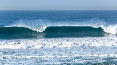 Mavi sudan oluşan okyanus dalgası sığ resif kumsallarına çarpıyor ve panoramik fotoğrafa bakıyor..