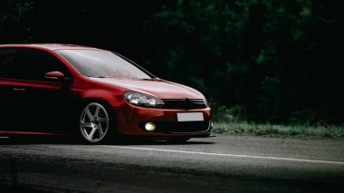 Yeşil ormanda kırmızı akortlu araba yolda.