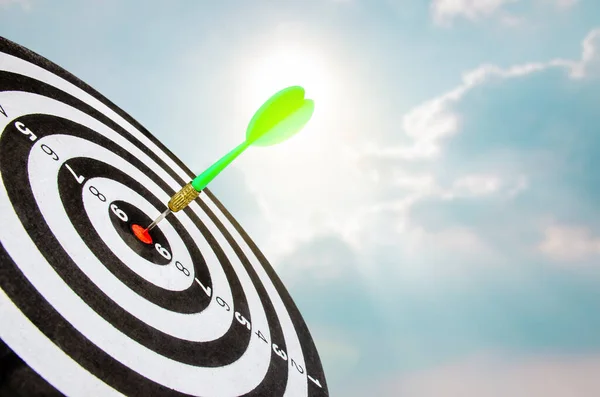Planning new business target and goals, Green dart arrow hitting in the target center of dartboard with sky and sun light background. achieve and victory concept