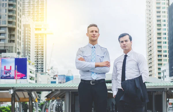 Portrait Of Two Businessmen standing side by side and crossing their arms and looking camera.