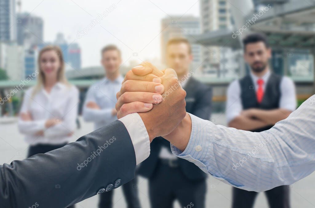 Close up of a business hand shake between two colleagues - greeting, dealing, merger and acquisition concepts and business people in the background