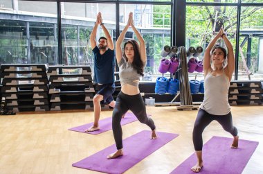Stüdyo konseptinde grup yogası, çeşitli çok ırklı sporlar eğitmen öğretmeniyle birlikte antrenman yapan ve savaşçı 1 pozunu tekrarlamaya çalışan insanlar.