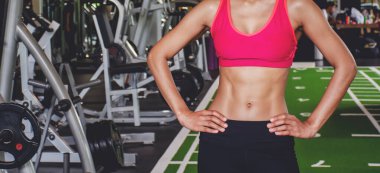 Spor salonunda bir kadının vücut geliştiricisinin yakın çekimi. Kaslı bir kadının portresi profesyonel jimnastik geçmişinde güçlü karın kasları gösteriyor, sporcu yoğun egzersize ara veriyor..