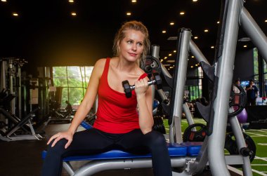 Salonda dambıl kaldırarak egzersiz yapan genç ve güzel bir kadın. Gülümseyen kızın sabah antrenmanının keyfini çıkarmasına sevindim. Çok çalışıyor.