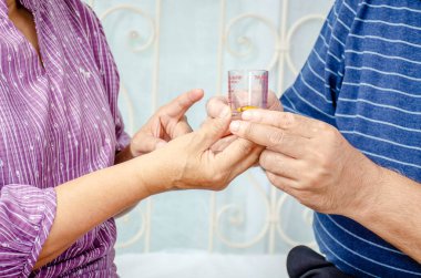 Hasta yaşlı bir adama destek olan ve kocasına hap veren yaşlı bir kadının elini kapat. İlaç vitamini takviyesi.