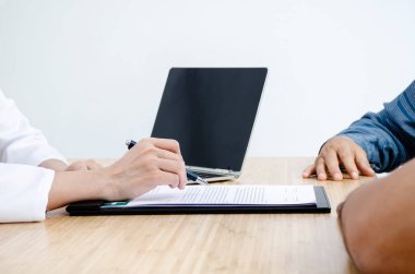 Doktor ve hasta bir şeyi tartışıyor ve notlar alıyor, sadece masada eller.