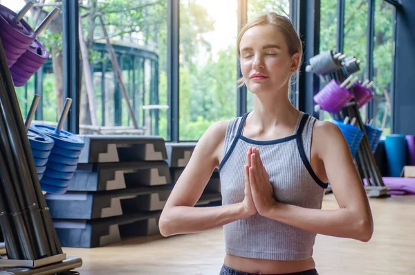 Genç çekici bir kadın yoga yapıyor, gözleri kapalı dinleniyor Padmasana 'da egzersiz yapıyor, yoga yapıyor, spor giyinen çekici bir kız evde ya da yoga stüdyosunda spor yapıyor.