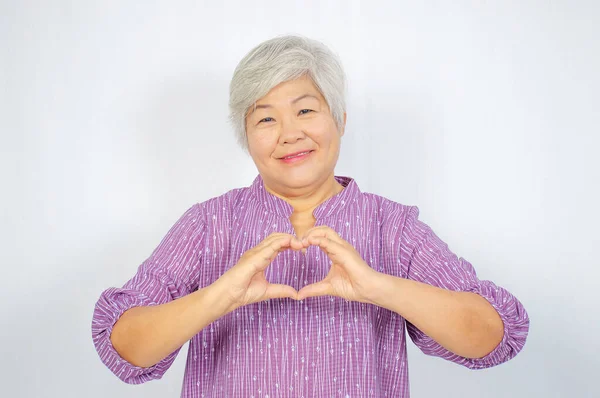 love and old people concept -  Happy senior woman showing hand heart gesture and smiling, take care of the health, or being in love