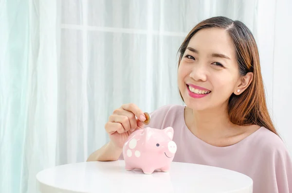 Mutlu Asyalı kadın para biriktirmek ve finansal konsept için domuzcuğa para koyuyor..
