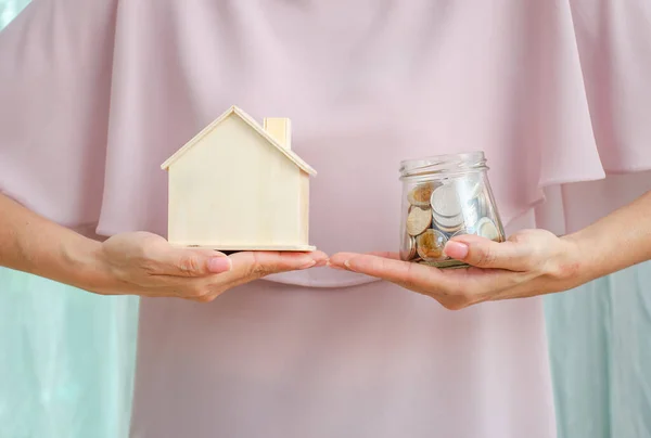 Loan or save for buy a house and real estate concept, Woman hand holding money  in glass jar and a model home