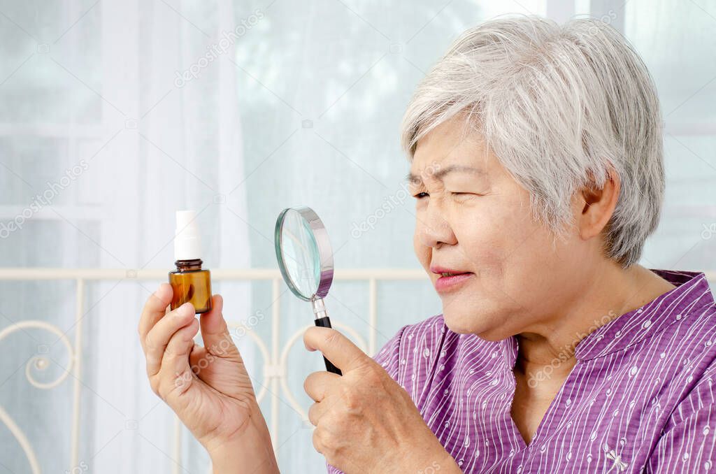 age, medicine, health care and people concept - Doubtful senior woman looking at medicine in his hand with Magnifying glass at home or hospital office