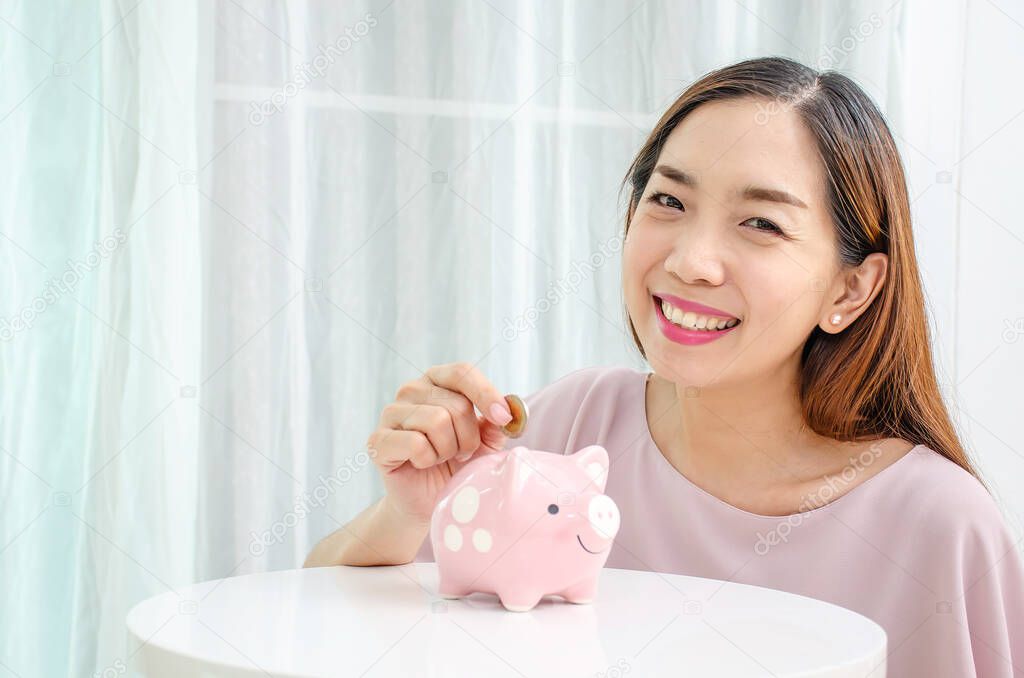 Happy asian woman putting money coin in to piggy for saving money wealth and financial concept.