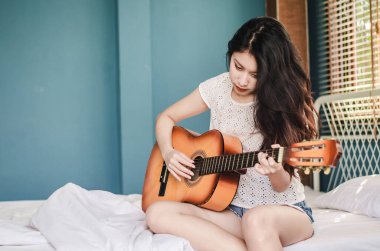 Sabahtan beri akustik gitarla çalan Asyalı kızın kısmi görüntüsü yatak odasında uyanıyor.