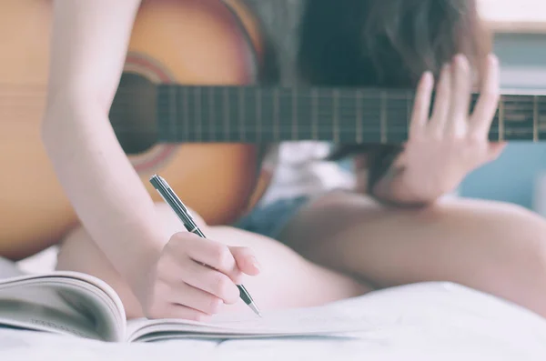 年轻美丽的女人坐在卧室的床上 拿着吉他 用课本 音乐家 作曲家 作曲家的概念创作歌曲和写歌 — 图库照片
