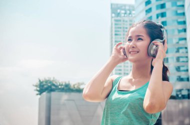 Spor giyim kuşağında güzel kadınlar açık havada güneşli bir günde antrenmandan sonra kulaklıkla müzik dinliyor. Güneşin tadını çıkaran ve akıllı telefondan kulaklıkla müzik dinleyen kız koşucu..