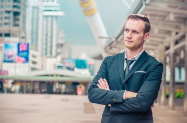 Başarılı takım elbiseli iş adamı ofis dışında elleri göğsünde duruyor, büyük şehir binalarına bakıyor, yeni projeler planlıyor, metin için alan kopyalıyor.