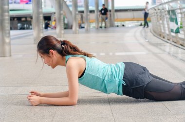 Genç kadın şınav çektikten sonra dinleniyor, kadın sokak şehrinde spor yapıyor.