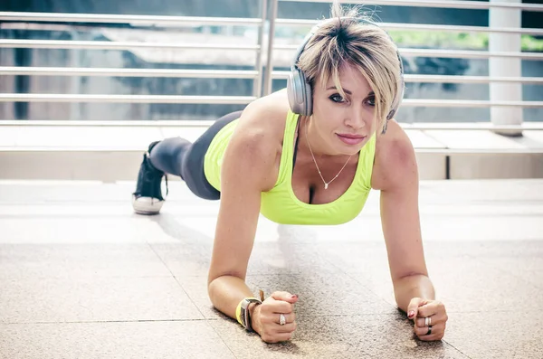 Close up to face of fit woman in sportswear doing plank exercise outdoor in the street city warm summer day. Concept of endurance and motivation.