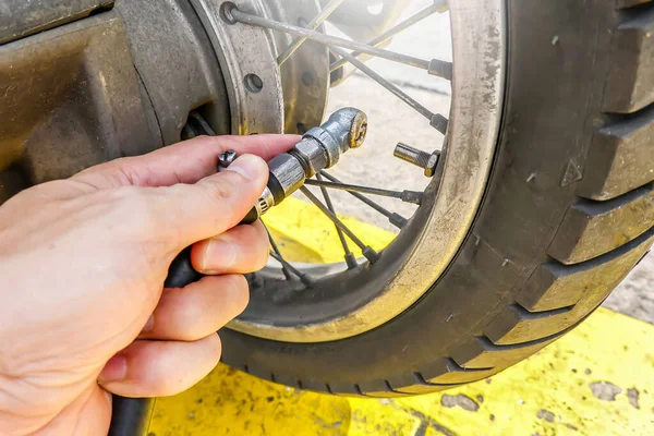 People hand are filling the tire pressure on the motorbike wheel from automatic air filler at filling station.Close-up.