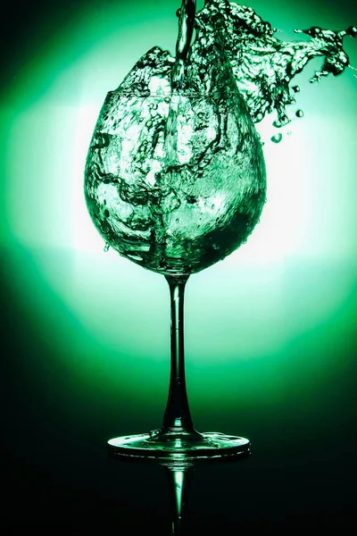 Pouring water into glass and splash out of a glass isolated on bright green and black background