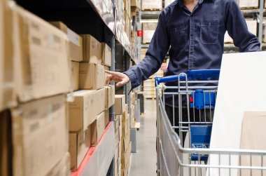 Alışveriş arabalı bir alıcı mağazada rafların arasında alışveriş merkezinin arka planında malları olan bir adam var.