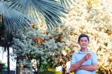 Asyalı son sınıf öğrencisi güneşli bir günde parkta durup kahve içiyor.